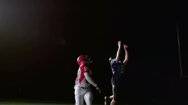 A football player catches a pass while a defender jumps to try and block it