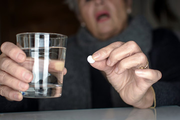 Senior older lady holding a tablet or pill in one hand and a glass of water in the other