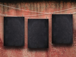 Three blank blackboard frames hanged by pegs against dirty red wall background