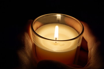 
Male hands holding a candle in the transparent glass shining in the darkness as a symbol of contemplation, meditation and calmness