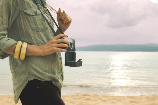 Fashionable woman holding camera on the beach.

