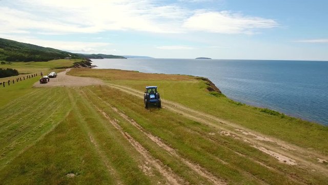 Aerial shot farmer cuts the grass on field by ocean cove