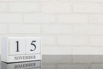 Closeup white wooden calendar with black 15 november word on black glass table and white brick wall...