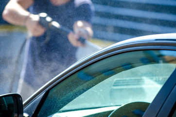 Man cleaning car at an auto shop with water vapor all over and a blue green reflection on the window