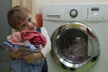 Happy cute little girl with clothes doing laundry in home interior