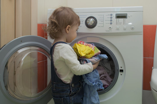 Small Child Puts Laundry In The Washing Machine. Mother's Helper. 2 Year Old.