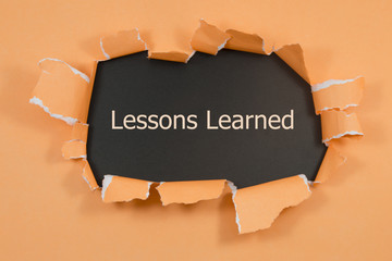 The word lessons learned appearing behind torn paper. 