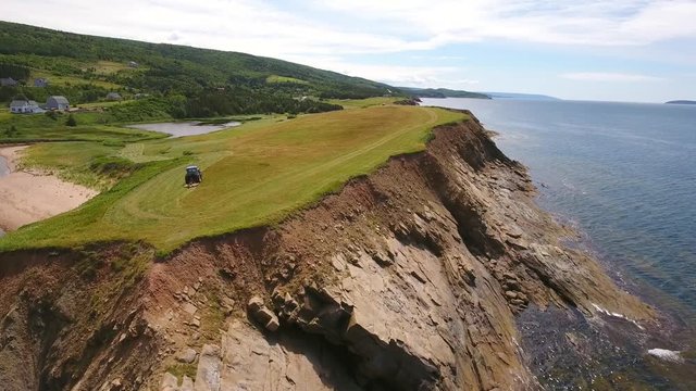Aerial rotating shot as farmer cuts grass on a field by ocean cove