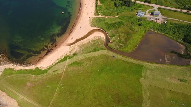 Aerial high shot of a farmer cutting grass on a field by ocean cove