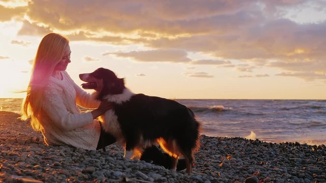 Young woman with long blond hair playing with his dog. Sitting on the beach at sunset and orange sky