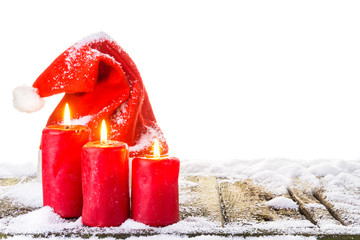 Weihnachtsmütze und 3 brennende Kerzen auf verschneitem Holzboden vor reinweißem Hintergrund