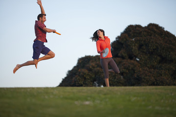 Couple laughing and running while playing frisbee at a park in San Diego, California. 