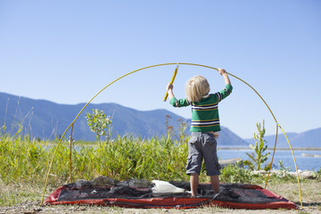 Little boy, age 6 setting up a tent during summertime on the shoreline of Lake Pend Oreille, Sandpoint, Idaho.