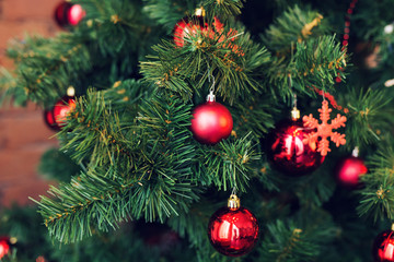 Closeup of red baubles hanging from a decorated Christmas tree.