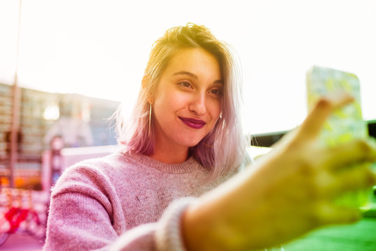Young beautiful caucasian purple grey hair woman outdoor in the city outdoor in city back light taking selfie with smart phone hand hold - vanity, social network, sharing concept