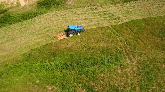 Aerial shot a farmer cutting grass on a field by ocean cove