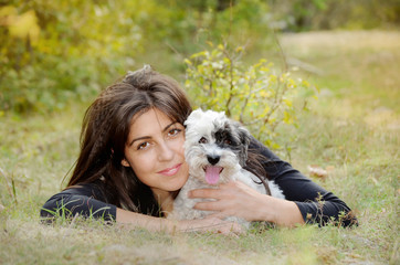 smiling woman laying on a meadow with her small havanese dog