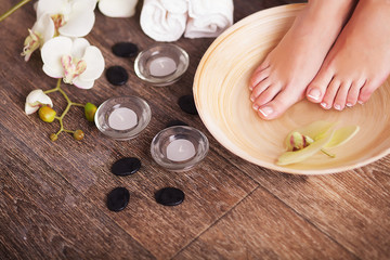 Naklejka na ściany i meble Female feet with drops of water, spa bowls, towels, flowers and candles.