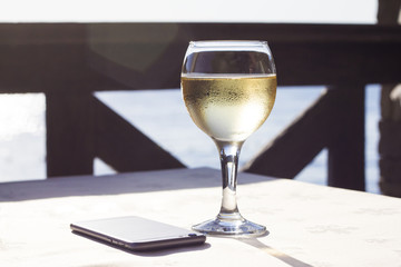 Glass of white wine and mobile on a table at sunset on the sea