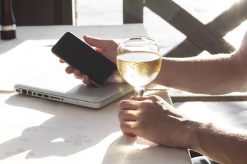 Cropped image of hand with telephone and glass of wine near the sea.
