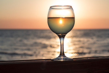 Glass of white wine on the background of the sea at sunset