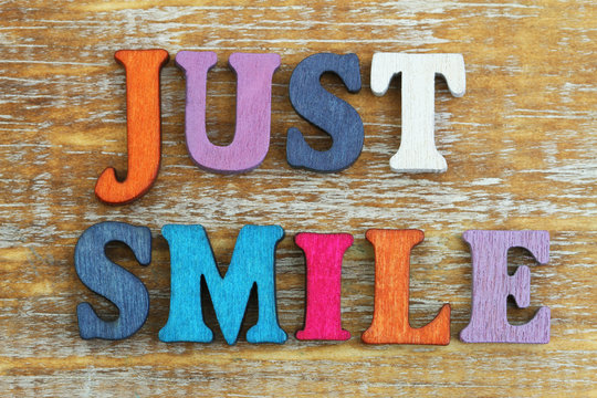 Just smile written with colorful letters on rustic wooden surface
