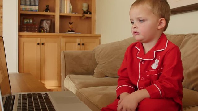 A little boy in Christmas pajamas watches show on computer