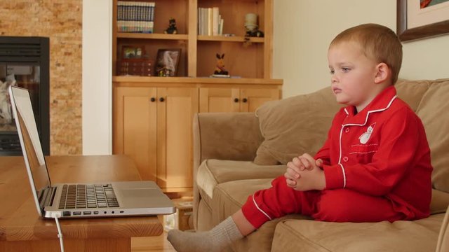 Little boy in Christmas pajamas watches show on computer