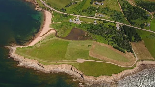Aerial high shot of farmer cutting grass on field by ocean cove