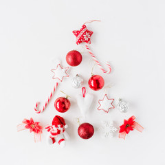 creative arrangement of bright red christmas tree made of christmas ball, sweets, toys on white background. flat lay, top view