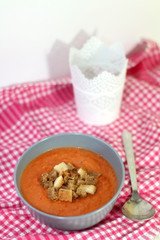 Gazpacho in a bowl with bread pieces on red checkered napkin. Selective focus.

