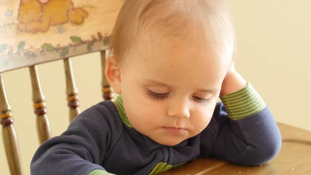 Adorable baby boy eating cereal in his highchair in kitchen
