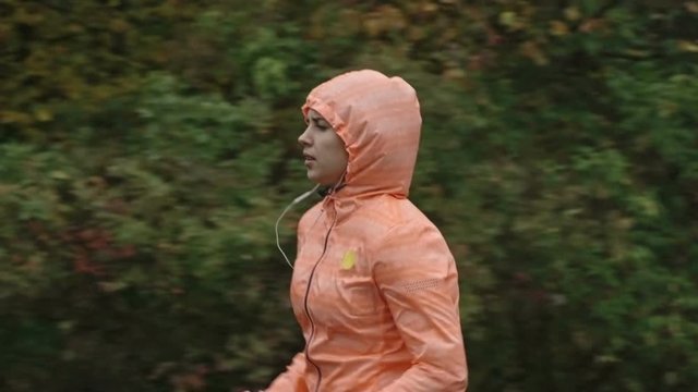 Medium closeup shot of woman in running jacket training in the rain outdoor in slow motion