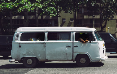 Side view of retro vintage white van car on the road with sleeping tired brazilian people inside, waiting green traffic light, sunny day, Rio de Janeiro, Brazil