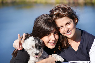 two sisters hugging her small white poodle dog.Family time