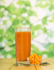 Glass juice and bowl sea-buckthorn berries on green abstract.