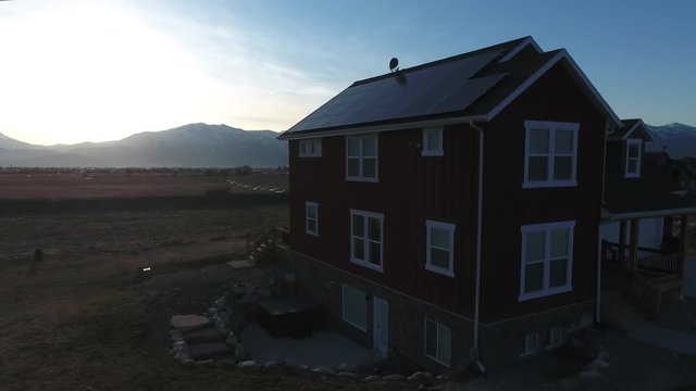 An aerial shot of a house with solar panels and mountains at sunset