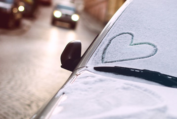 Heart drawn on a car windscreen covered with snow