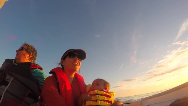 A family rides a boat on the ocean coastline at sunset