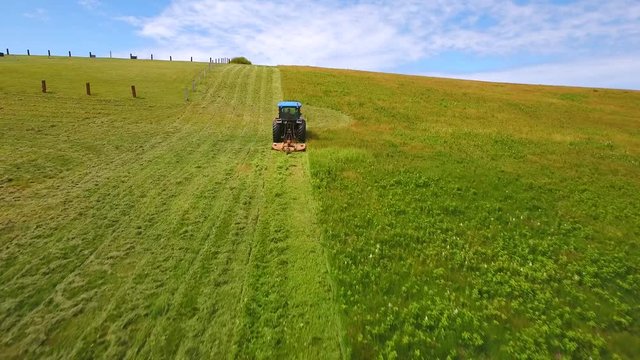Aerial farmer cuts the grass on field by ocean cove