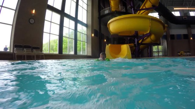 Boy goes down the waterslide in pool
