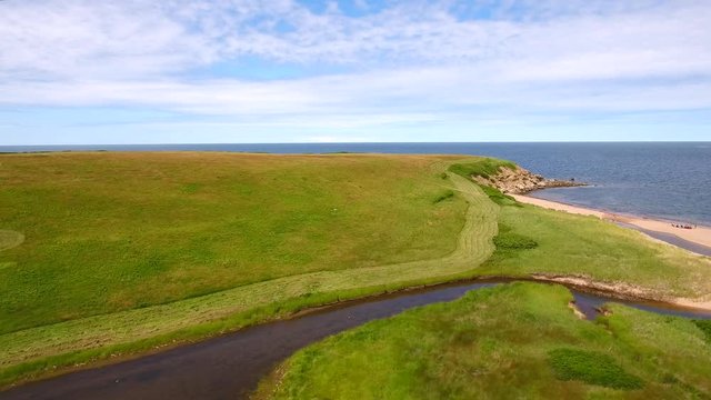 Aerial farmer cuts grass on field by ocean cove