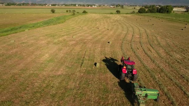 Aerial shot as tractor cuts and bails hay