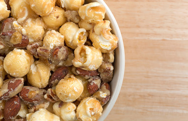 Gourmet popcorn with nuts in a bowl top close view on a wood table.