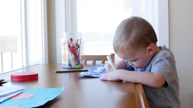 A cute little boy makes and colors a helicopter on paper