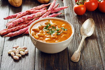 Bean soup in white bowl surrounded by ingredients on wooden table