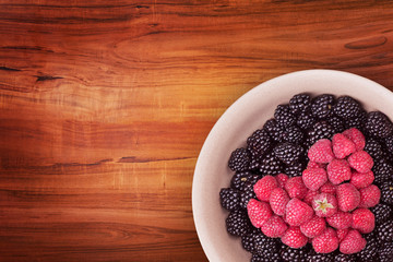 Ceramic plate with heart shaped berries on the right bottom corner of the wooden table with clipping path. Top view.