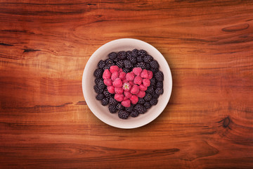 Ceramic plate with heart shaped berries on the middle of the wooden table with clipping path. Top view.