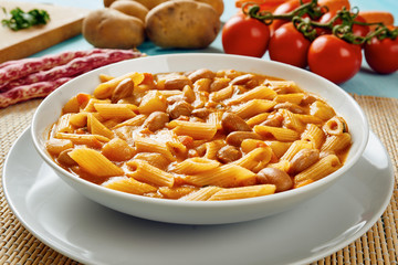 Fototapeta na wymiar Pasta with beans in white dish, potatoes, carrots, tomatoes in background