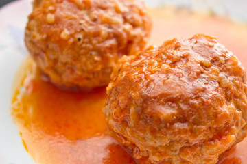two meatballs in tomato sauce on a white plate